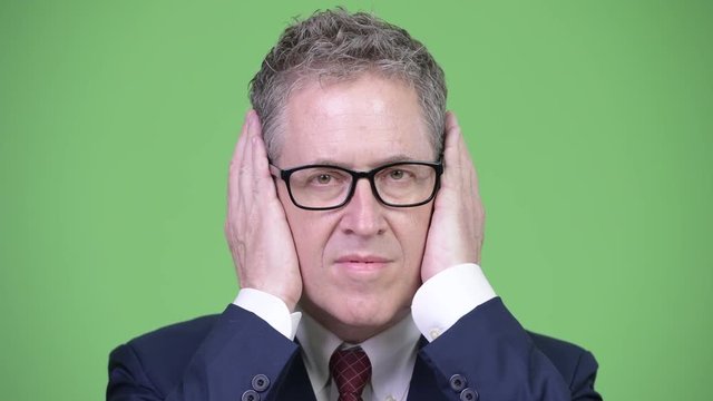 Head shot of mature businessman covering ears as three wise monkeys concept
