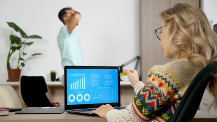 Woman studying company data analysis on animated chart while her husband is making a lot of noise in the background watching TV. Freelancer working at home. Dolly slider 4K footage - Powered by Adobe