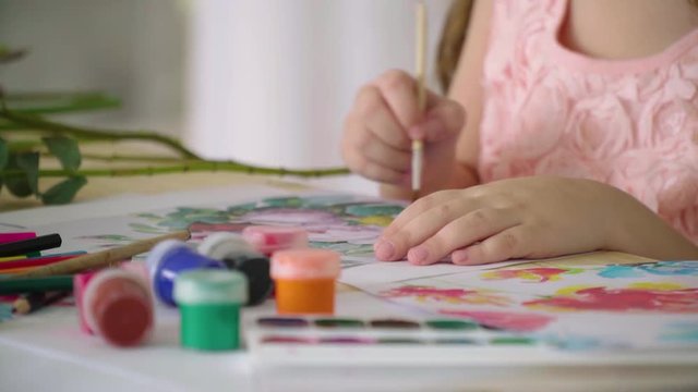 A girl in a pink dress draws flowers with a brush, slow motion