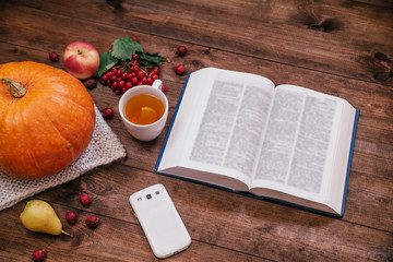 Top view of a  pumpkin, apples and a book, phone on wooden table.