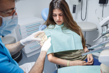 Professional doctor demonstration process of healthy teeth brushing to young woman sitting in chair. 