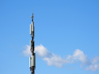 Cellular tower on the blue sky with some clouds background