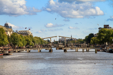 Naklejka premium Piękny widok na chudy most (magere brug) nad rzeką Amstel w Amsterdamie w Holandii w słoneczny letni dzień z chmurami i ptakami