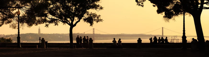 Wunderschönes Panoramabild von Silhouetten mit Blick auf die Brücke Ponte 25 de Abril und das Heiligtum von Christus dem König (Cristo Rei) bei Sonnenuntergang von der Burg Sao Jorge in Lissabon, Portugal © dennisvdwater