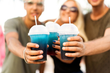 three friends cheerful company rest on a tropical beach and drink cocktails, very, magazine concept