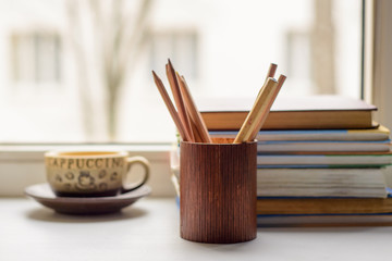 Cup of coffee, books, pencils in the pencil box on the windowsill in the morning