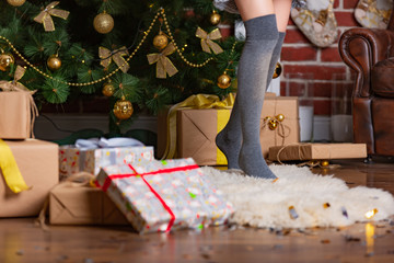 woman stands on tiptoe in a warm gaiters on a fur rug in the room near the Christmas tree with presents
