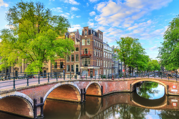 Beautiful view of the iconic UNESCO world heritage Prinsengracht and Reguliersgracht canals in Amsterdam, the Netherlands, on a sunny summer morning with a blue sky and reflection
