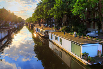 Houseboats at the UNESCO world heritage canals of Amsterdam, The Netherlands, on a sunny summer morning with a blue sky and clouds and a mirror reflection