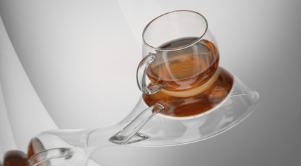 transparent tea cup on the reflective surface on a light gray background. distorted reflection