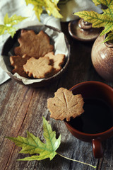 Autumn mood. Cinnamon cookies in form of maple leaves, cup of coffee and yellow leaves. Toned image
