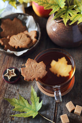 Autumn mood: cinnamon cookies in form of maple leaves, tea, red apple and yellow leaves