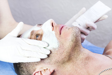 Naklejka premium A man does the procedure cleaning his face with a clay mask in the beauty salon 
