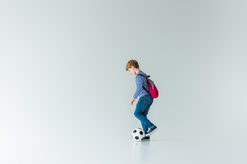 Fototapeta na wymiar side view of schoolboy with backpack playing with fotball ball on white