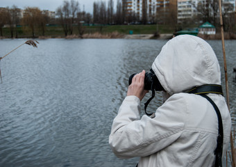A girl in a white jacket takes pictures of nature near the lake
