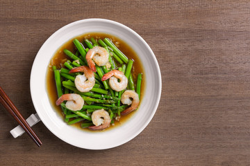 top view of stir fried asparagus and shrimp with oyster sauce in a ceramic dish on wooden table. asian homemade style food concept.