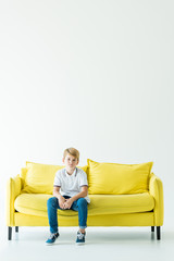 Obraz premium adorable boy sitting on yellow sofa and looking at camera on white