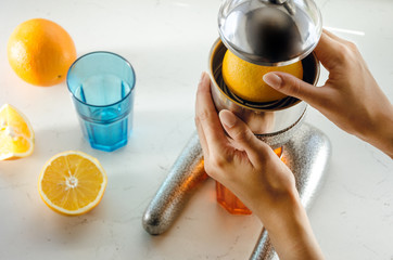 Close up of young woman hands doing fresh lemonade, squeezing juice from citrus fruit, juicer