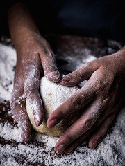 pastry chef hand kneading Raw Dough with sprinkling white flour over kitchen table.