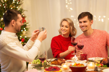 holidays and celebration concept - happy man photographing his friends at christmas dinner
