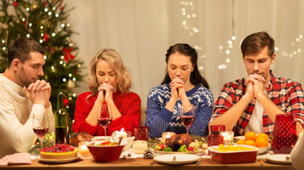 holidays and celebration concept - friends holding hands and praying before christmas dinner at home