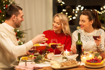 holidays and celebration concept - happy friends having christmas dinner at home, eating and drinking