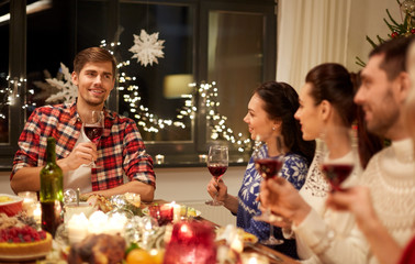 holidays and celebration concept - happy friends with glasses of wine having christmas dinner and speaking toast at home