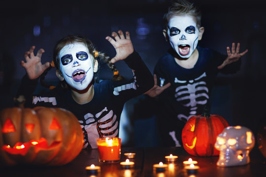 happy Halloween! children in costume of skeletons with pumpkins and candles in dark.
