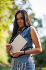 Young pretty brunette girl with the tablet and listening to music on the street in summer.