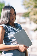 Young pretty brunette girl with the tablet and listening to music on the street in summer.