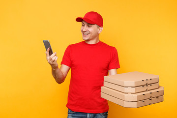 Delivery man in red cap t-shirt giving food order italian pizza in empty flatbox boxes on yellow background. Male employee pizzaman courier doing taking selfie shot on mobile phone. Service concept.