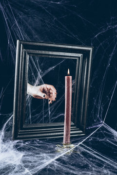 Cropped View Of Mystic Hand Taking Candle From Mirror Frame With Scary Spider Web Around