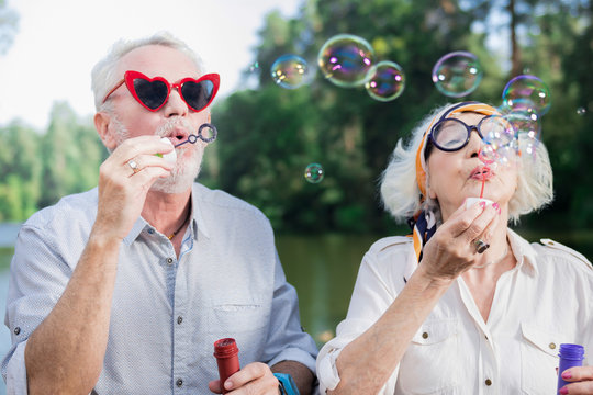 Soap bubbles. Funny active couple of pensioners standing on the bridge and blowing soap bubbles