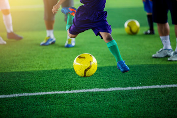 Kid soccer player shoot yellow ball on green artificial turf.