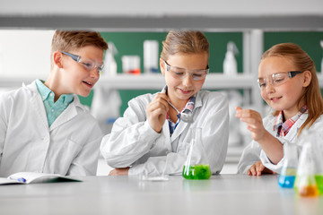 education, science, chemistry and children concept - kids or students with test tube making...