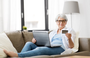 technology, online shopping and people concept - happy senior woman in glasses with laptop computer and credit or bank card at home