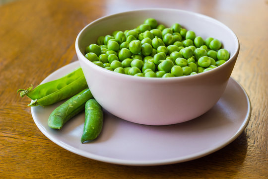 pink bowl with green peas and three pea pods lie near