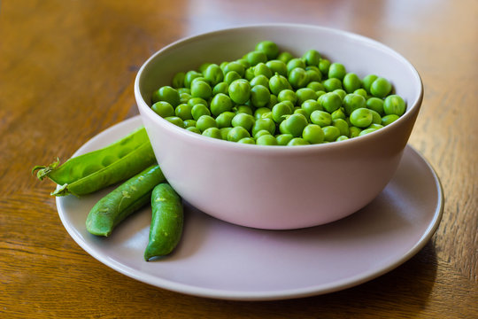 pink bowl with green peas and three pea pods lie near