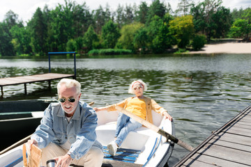 Relaxing in boat. Confident active senior couple thoughtfully sitting in the boat and looking ready to start their trip