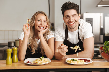 Emotional excited young friends loving couple chefs on the kitchen eat tasty pasta.