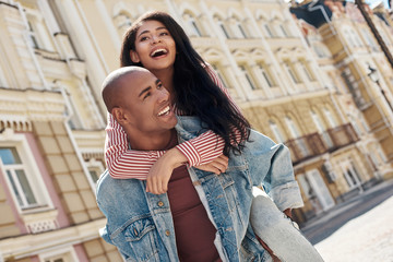 Romantic Relationship. Young diverse couple walking on the city street boyfriend carrying girlfriend on back laughing happy