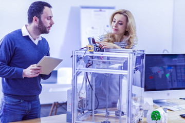 3D printer. Serious woman standing at her workplace while testing modelling gadget