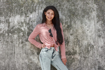 Young brunette girl standing on grey wall posing to camera smiling cheerful