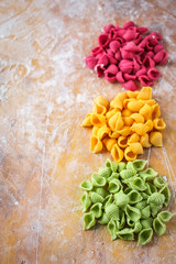 Fototapeta na wymiar raw colored pasta on the kitchen wooden table with flour, top view