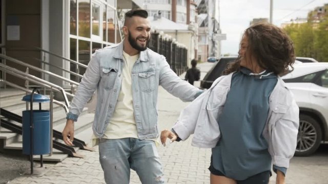 Excited young couple having fun and dancing while walking on street in summer
