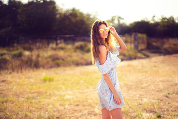 Obraz premium beautiful young woman in dress and sunglasses having fun with hair outdoor in countryside on a warm summer day