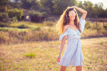 Fototapeta na wymiar beautiful young woman in dress and sunglasses having fun with hair outdoor in countryside on a warm summer day