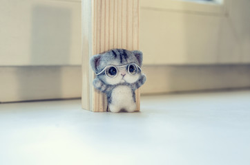 Felting toy gray kitten near a wooden bar