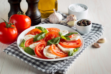 Photo of Caprese Salad with tomatoes, basil, mozzarella, olives and olive oil on wooden background. Italian traditional caprese salad ingredients. Mediterranean, organic and natural food concept.