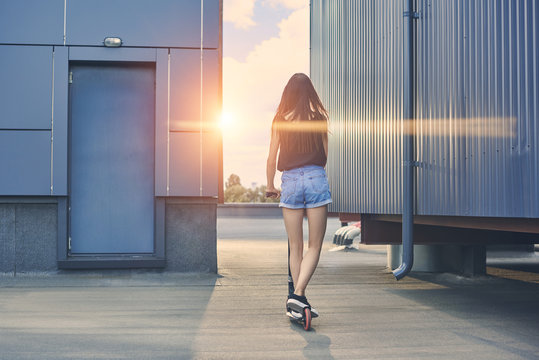 Back View Of Young Woman Riding Scooter On Roof With Sunbeams